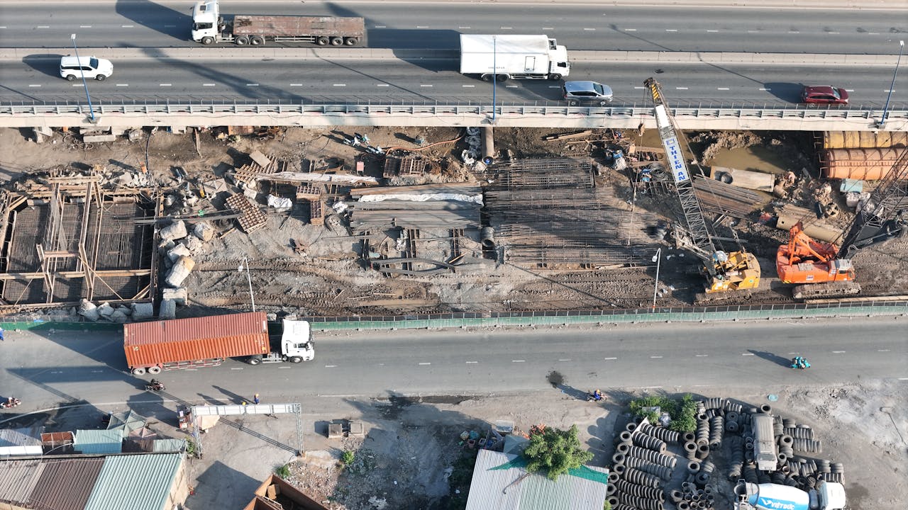 Aerial shot of a bridge construction site with vehicles passing on the highway above.